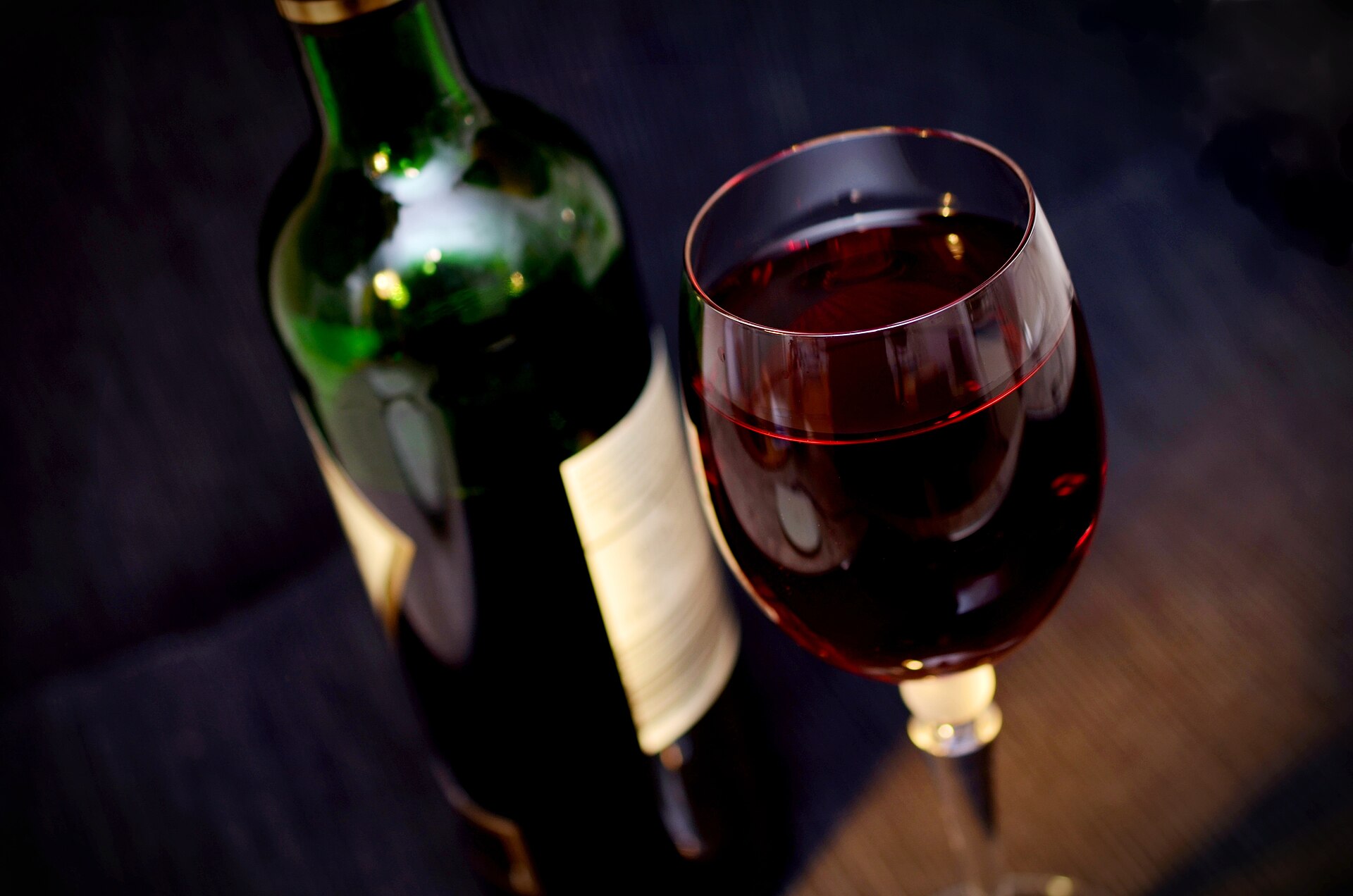 Botella y copa de vino tinto sobre fondo oscuro